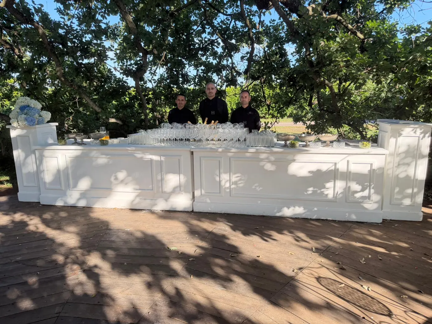 Lunghi banchi buffet bianchi allestiti sotto le querce di un giardino